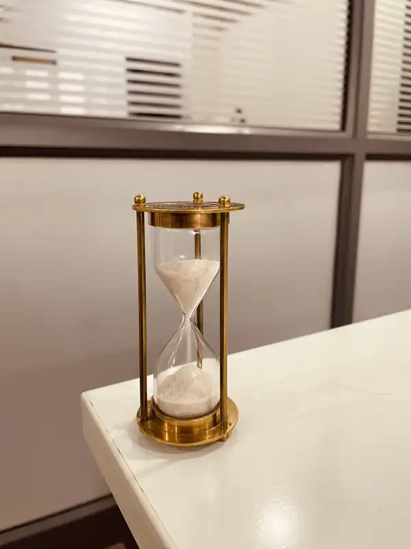 A brass hourglass with white sand standing on the corner of a white counter